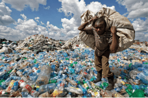 Plastic treaty (900 x 600 px) A man walks on a mountain of plastic bottles as he carries a sack of them to be sold for recycling after weighing them at the dump in the Dandora slum of Nairobi, Kenya