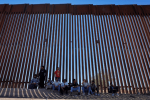 Immigration policy 600x900 A group of people sit in the shade of the U.S. Mexico border wall