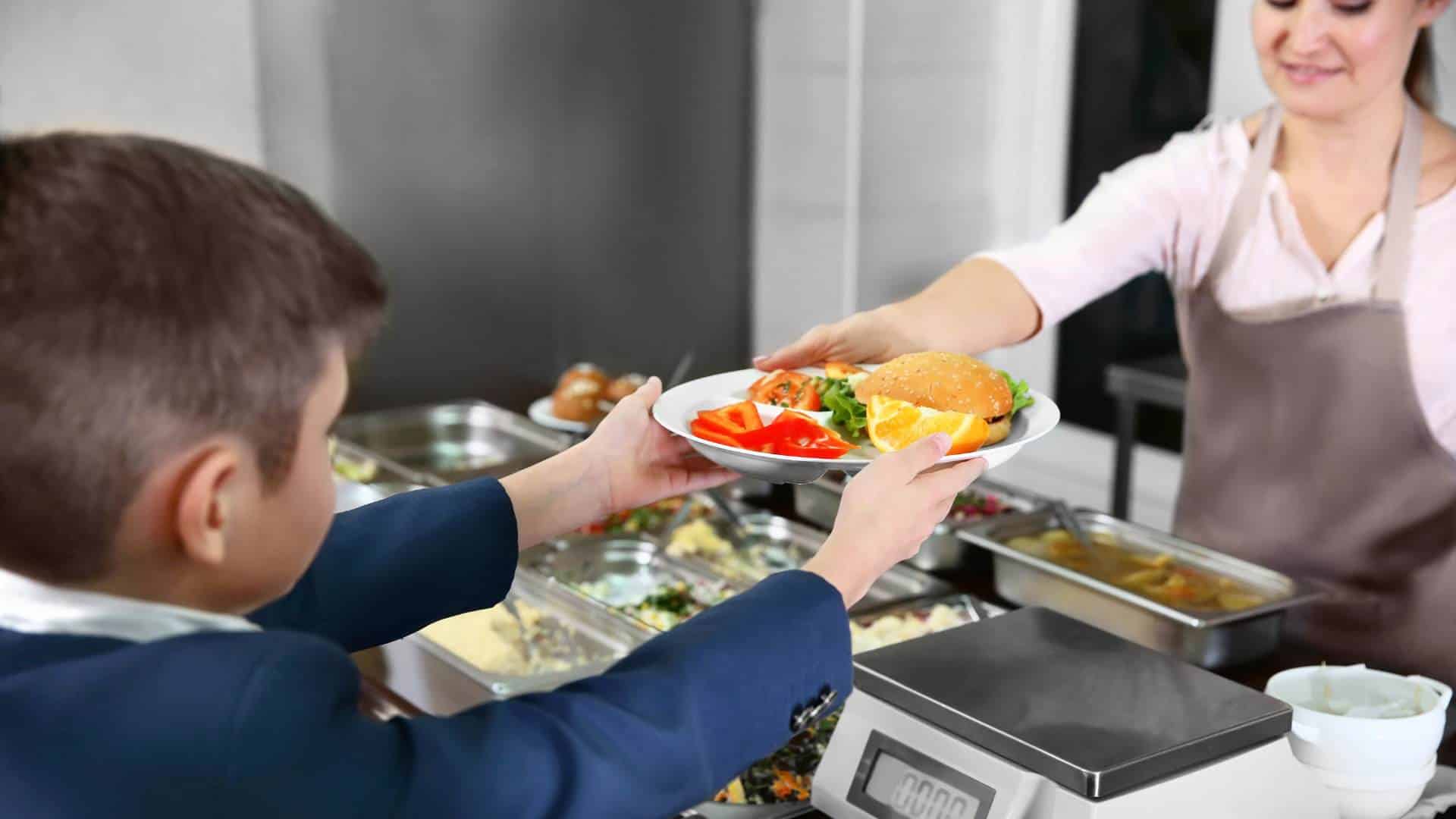 Woman serves lunch to a boy in a cafeteria<br />

