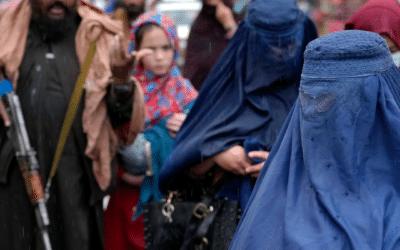 Afghan women walk through the old market as a Taliban fighter stands guard, in downtown Kabul, Afghanistan.