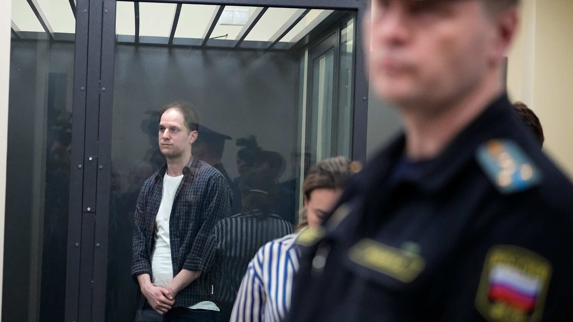 Wall Street Journal reporter Evan Gershkovich, left, stands in a glass cage in a courtroom at the First Appeals Court of General Jurisdiction in Moscow