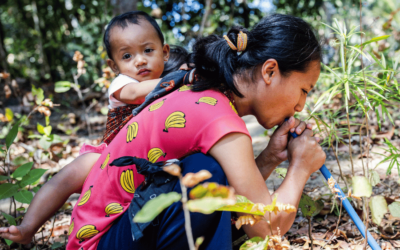 A woman holds her child while sucking water from a hose