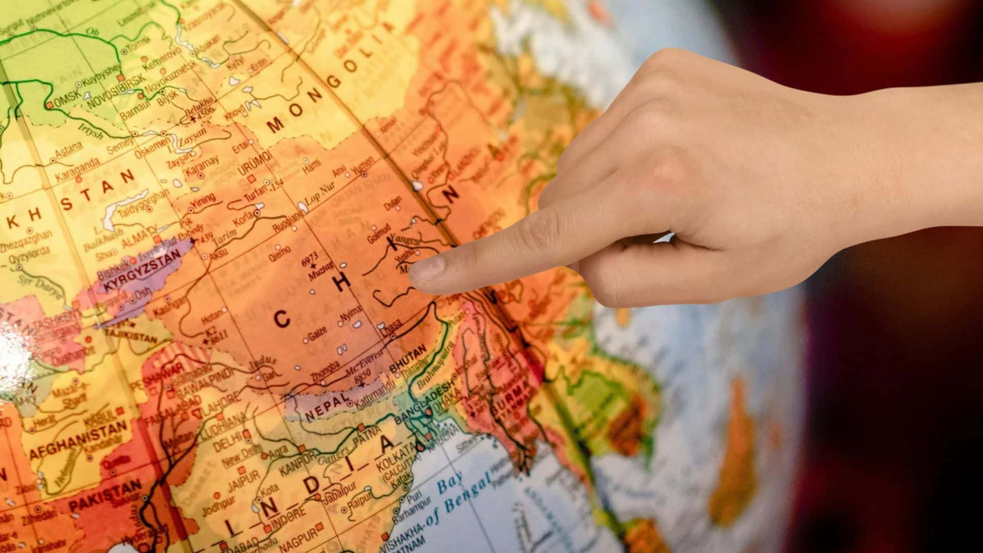 A finger points to China on a globe. 
